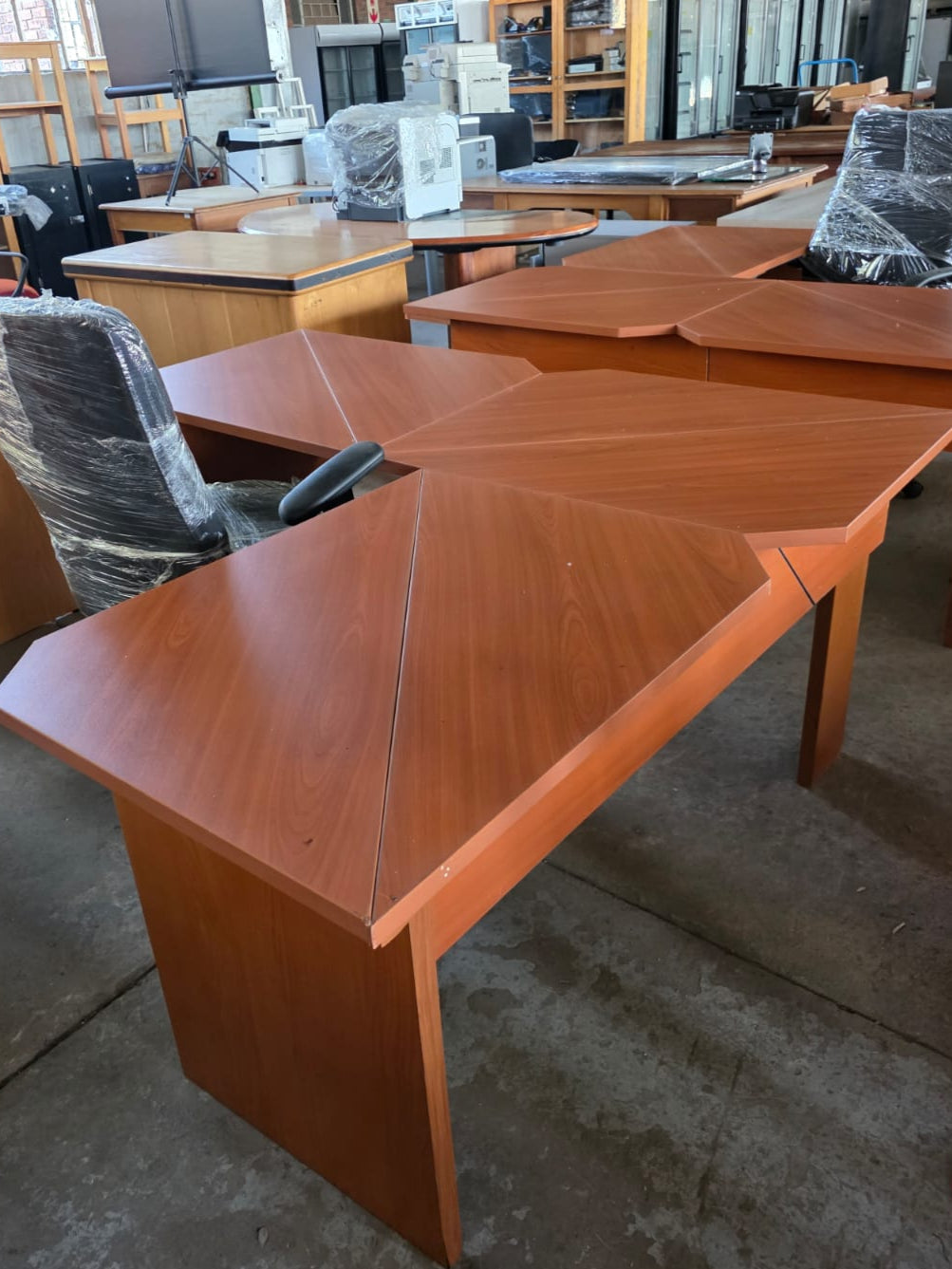 Wooden office desk in a warehouse setting with chairs and other furniture.